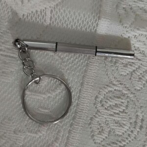 May include: A silver keychain with a small screwdriver attached to a silver key ring.