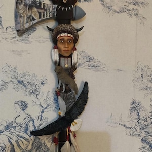 May include: A decorative tomahawk with a wooden handle and a metal blade. The blade is decorated with a wolf, a bear, a Native American, an eagle, and feathers.