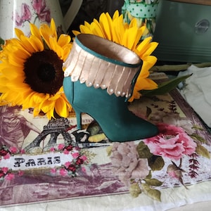 May include: A green boot with a gold trim and a high heel. The boot is sitting on a floral patterned surface with the word "Paris" printed on it.