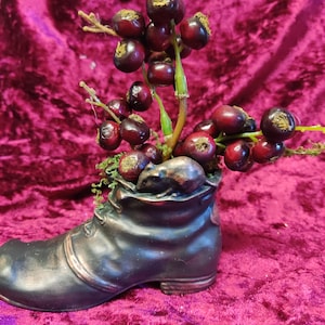 May include: A small, dark brown boot with a mouse figurine inside. The boot is filled with red berries and green leaves.