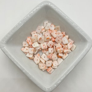 May include: A bowl of white and orange shell beads. The beads are square shaped with a hole in the center.