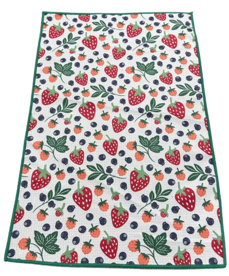 Puede incluir: Una toalla de cocina blanca con un borde verde presenta un patr&oacute;n repetido de fresas rojas, hojas verdes y peque&ntilde;as bayas azules y naranjas.