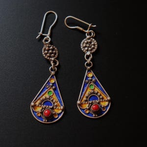 May include: A pair of silver dangle earrings with blue, yellow, green, and red enamel. The earrings feature a teardrop-shaped design with intricate details.