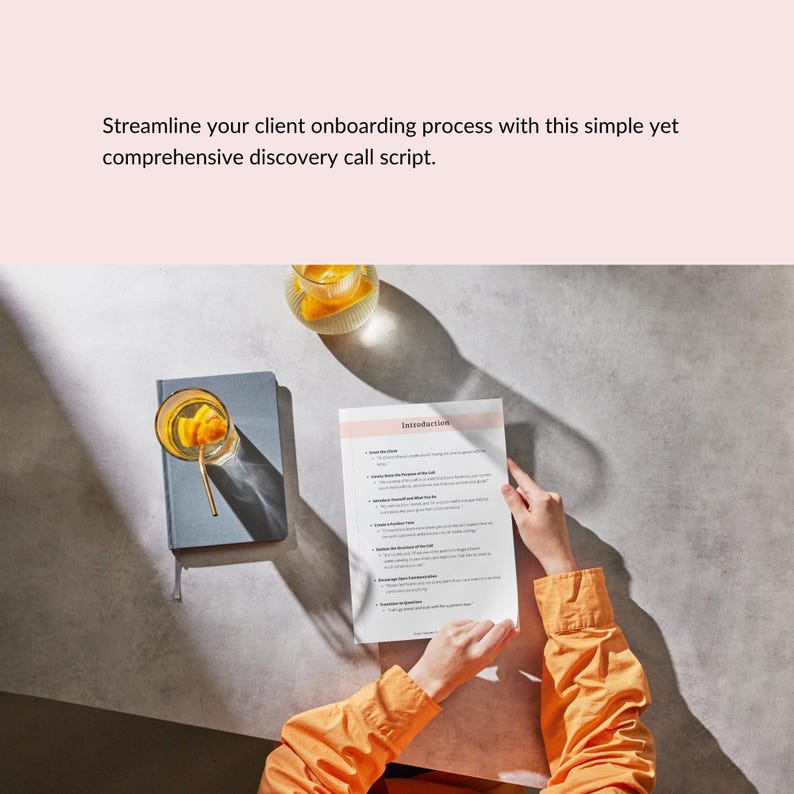 May include: A top-down view shows a grey notebook, a glass of orange-infused beverage with a gold straw, and a document titled "Introduction." The document is being held by a person wearing an orange shirt. The text at the top says "Streamline your client onboarding process with this simple yet comprehensive discovery call script."
