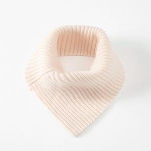 May include: A light peach-colored, ribbed knit scarf. The scarf is a triangular shape, designed to be worn around the neck. The fabric has a soft, textured appearance.
