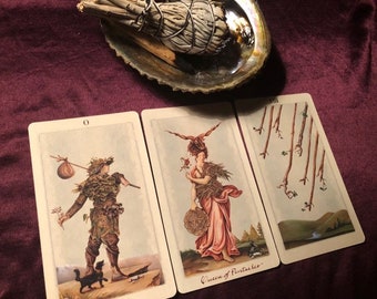 Puede incluir: Tres cartas de tarot sobre una superficie burdeos. Las cartas son de la baraja de tarot 'Wild Unknown'. Las cartas son 'El Loco', 'Reina de Pentáculos' y 'Ocho de Bastos'.