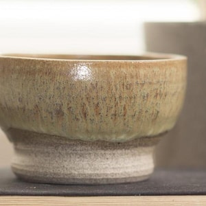 May include: A small, round, ceramic bowl with a light green glaze and a white base. The bowl has a speckled, textured surface.