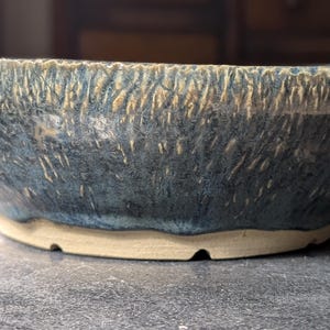 Peut inclure: Un bol en céramique bleu et brun avec une surface texturée. Le bol a un bord large et une base arrondie.