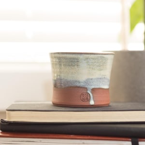 May include: A ceramic mug with a light blue and brown glaze. The mug is sitting on top of a stack of notebooks.
