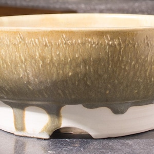 May include: A handcrafted ceramic bowl with a wide, shallow design. The bowl features a textured, light brown exterior with a white base. The base has a unique shape with cut-out sections. The bowl is approximately 30 cm in diameter.