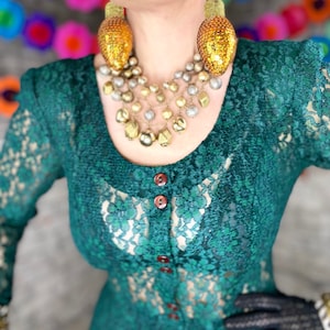 Può includere: Un abito in pizzo verde acqua con una collana di perline dorate e argentate e grandi orecchini di paillettes dorate.
