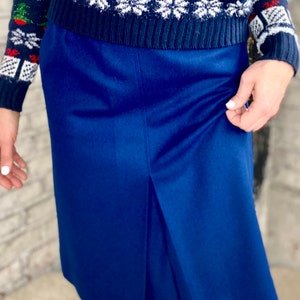 May include: A dark blue skirt with a front slit. The skirt is knee-length and has a smooth, polished finish.