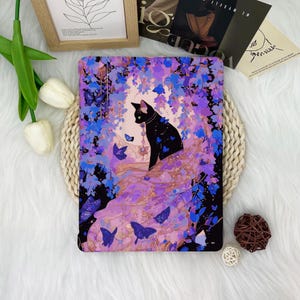 May include: A black cat with a purple flower crown sits on a purple and pink floral background. The cat is surrounded by butterflies and vines. The background is a dark purple and black.