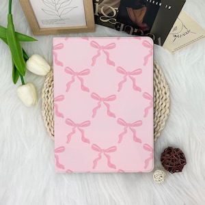 May include: A pink tablet case featuring a repeating pattern of light pink bows. The bows are watercolor-style, adding a soft, feminine touch to the design. The case is rectangular and likely designed to protect a tablet.