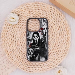 Könnte beinhalten: Schwarz-weißes Handycase mit Ghostface-Motiven und roten Herz-Akzenten. Der Schriftzug "ghost face" ist auf dem Case abgebildet. Es liegt auf einer geflochtenen, beigen Unterlage mit weißen Blumen.