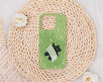 May include: A green phone case featuring a playful black cat and a white cat design. The case has a light green background with small white flower accents. The phone case is on a woven, circular mat.