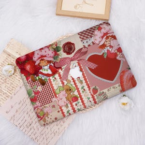 May include: A decorative laptop case featuring a patchwork design with Strawberry Shortcake characters, strawberries, and a red heart. The case has a red and white gingham ribbon and a red wax seal. The Apple logo is visible.