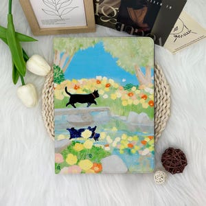 May include: A black cat walks through a field of colorful flowers towards a pond. The pond is surrounded by green grass and trees. The background is a blue sky with white clouds.