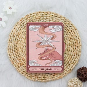 May include: A pink tarot card with a white star and a hand holding a flowing ribbon. The card is labeled "XVII THE STAR".