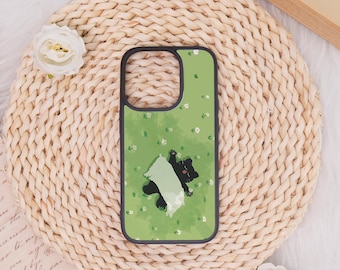 May include: A green phone case featuring a black cat illustration with a white blanket, set against a background of small white flowers. The case has a black border and is displayed on a woven, beige surface.