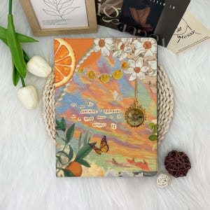 May include: A colourful notebook cover featuring a collage of images, including a compass, flowers, oranges, and a butterfly. The text on the cover reads "It's not all sunshine & rainbows but a good amount of it actually is."