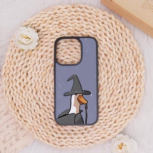 May include: A phone case featuring a cartoon goose wearing a wizard hat and cloak in the rain. The case has a black border and a light blue background with white rain streaks. The goose has an orange beak and is holding a staff.
