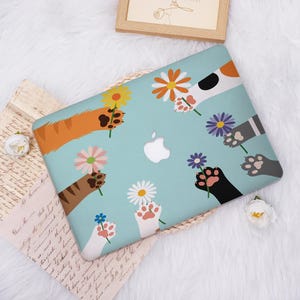 May include: A light blue laptop case featuring a design of various cat paws holding colorful flowers. The paws are in shades of orange, brown, black, gray, and white. The Apple logo is visible in the center.