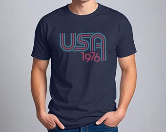 May include: A navy blue t-shirt with a retro-style graphic of "USA 1976" in red and blue.