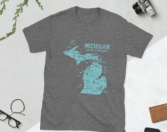 May include: A heather grey t-shirt with a blue outline of the state of Michigan. The shirt features the text "MICHIGAN The Great Lakes State" and a map of the state with major cities and landmarks.