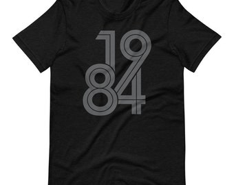 May include: Black t-shirt with the number "1984" printed in gray. The numbers are in a retro, bold font style. The shirt is made of a soft material and has short sleeves and a crew neck.
