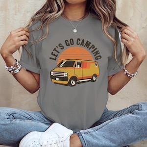 Może przedstawiać: Szary T-shirt z grafiką w stylu vintage przedstawiającą żółty van i napis "Let's Go Camping".