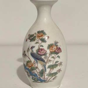 May include: A white ceramic vase with a gold rim. The vase features a colorful illustration of a bird perched on a branch with flowers. The bird has blue, green, and yellow feathers. The flowers are pink, orange, and yellow.