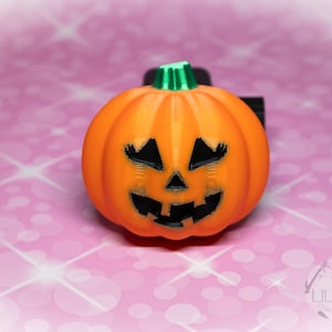 May include: Orange plastic jack-o'-lantern with a black smiling face. The pumpkin is on a pink background with a white sparkle pattern.