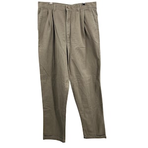 May include: Khaki-coloured pleated trousers hanging against a white background. The trousers have a button closure and a zip. The trousers are made of a durable fabric and have a classic, relaxed fit. The trousers are a neutral colour.