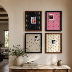 May include: Four rectangular wall frames with fabric backings in black with white floral stripes, pink with red patterns, beige with black floral motifs, and white with yellow floral stripes, each displaying a single small square photograph.