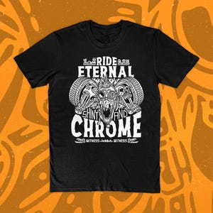 May include: Black t-shirt with a white graphic featuring a skull with tires and the words "RIDE ETERNAL SHINY AND CHROME". The design includes the word "WITNESS" at the bottom. The shirt is displayed on an orange background.