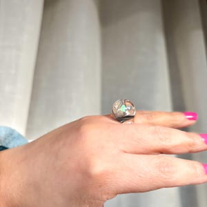 May include: A silver ring with a clear stone and a green stone set in a geometric design.