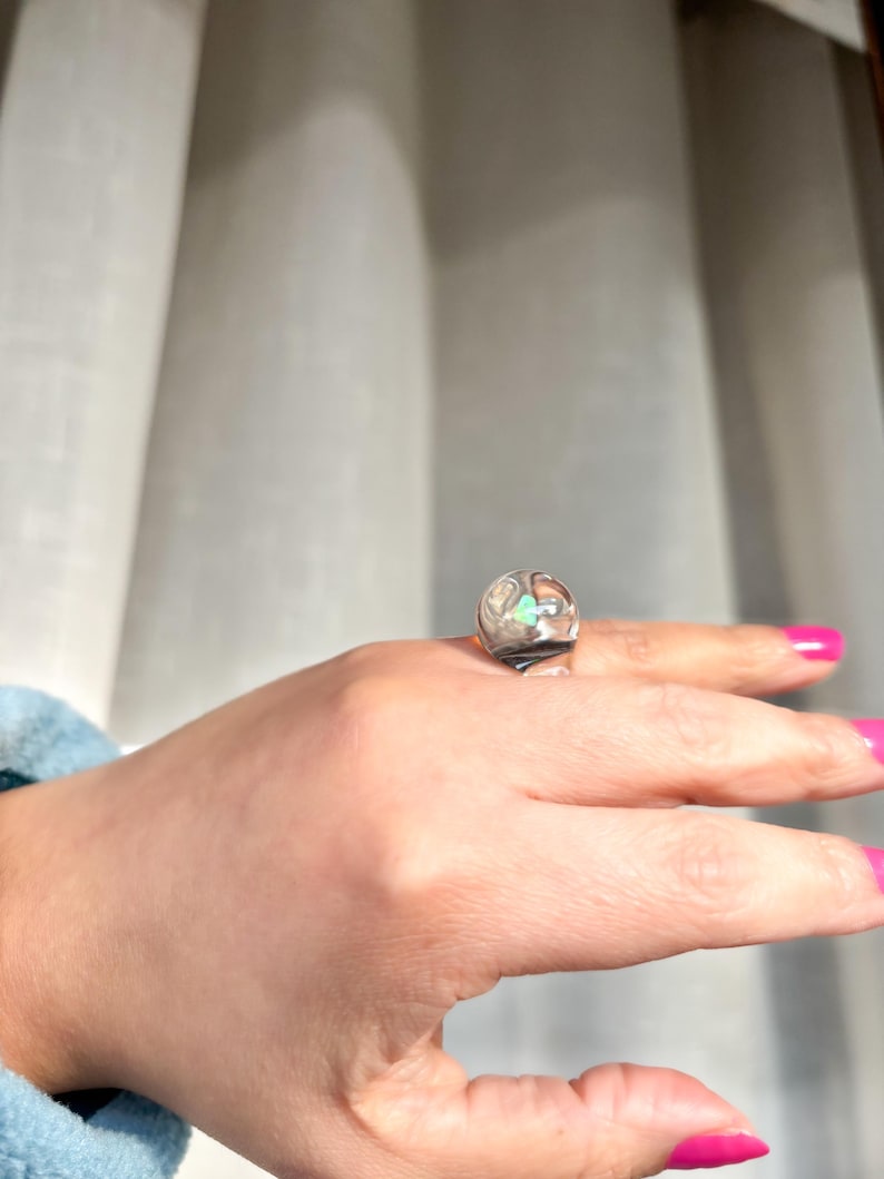 May include: A silver ring with a clear stone and a green stone set in a geometric design.