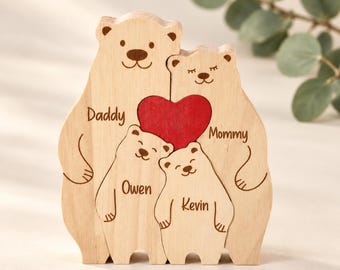 May include: A light-colored wooden bear family puzzle featuring four bear-shaped pieces. The two larger bears are labeled Daddy and Mommy, while the two smaller bears are labeled Owen and Kevin. A bright red wooden heart sits between the bears.
