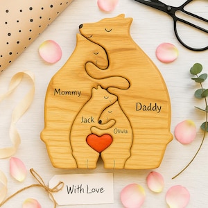 May include: Wooden family bear puzzle with the words "Mommy," "Daddy," "Jack," and "Olivia" engraved. A red heart is in the center. The words "With Love" are on a tag. Rose petals and scissors are in the background.