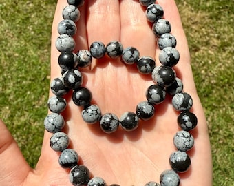 May include: Two black and white snowflake obsidian bracelets. The bracelets are made of round beads and are stacked on top of each other.