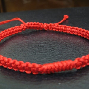 Puede incluir: Un brazalete de cuerda roja trenzada con cierre anudado.