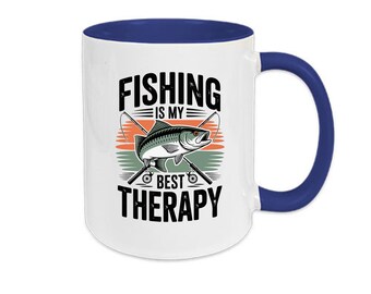 May include: White ceramic mug with a blue interior and handle. The mug features the text "FISHING IS MY BEST THERAPY" in black, along with a graphic of a fish and fishing rods. The design is set against a sunset-colored background.