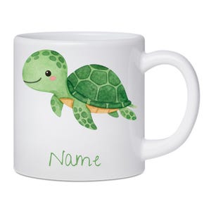 Può includere: Tazza in ceramica bianca con un'illustrazione di una tartaruga verde. La tartaruga ha un guscio a motivi e un viso sorridente. La parola "Name" è scritta in verde sul fondo della tazza. La tazza ha un manico bianco.