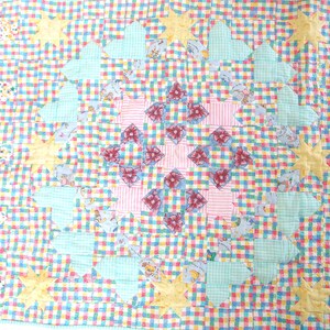 May include: A patchwork quilt with a central design of pink and red flowers surrounded by a ring of green and yellow stars. The quilt is made of a variety of fabrics, including gingham, floral prints, and solid colors.