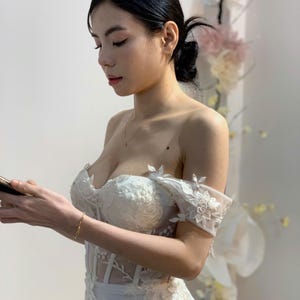 Elegant and modern ivory off-the-shoulder mermaid wedding dress with sparkling beading and a classic corset design that flatters the figure