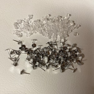 May include: A large quantity of silver earring posts and clear earring backs. The earring posts have a small round disc at the end. The earring backs are small and clear.
