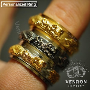 Könnte beinhalten: Ein Satz von vier stapelbaren Ringen mit einem Drachenmotiv. Die Ringe sind aus Gold und Silber gefertigt. Der oberste Ring ist aus Gold mit einem Drachenmotiv, der zweite Ring ist aus Silber mit einem Drachenmotiv, der dritte Ring ist aus Silber und der unterste Ring ist aus Gold mit einem Drachenmotiv. Die Ringe sind auf einem Finger gestapelt.