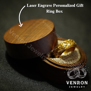 May include: A wooden ring box with a lid, the lid is open and a gold ring with an intricate design is inside. The box is made of dark wood and has a smooth finish. The ring is made of gold and has a detailed design. The box is labeled "Venron Jewelry".