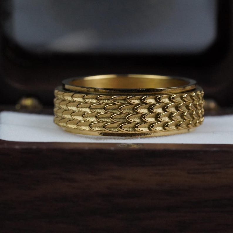 May include: A gold ring with a textured, scaly design. The ring is made of metal and has a shiny finish.